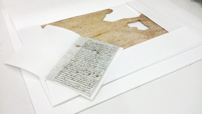Un document de pergamí i un document de paper protegits amb camises de paper de conservació de pH neutre